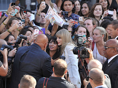 Taylor Swift taking a photo with a fan in a large crowd.