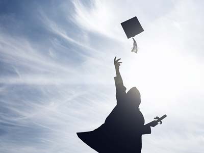 A person in graduation regalia throwing their cap into the air.