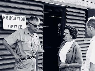 Black and white photo of three people standing next to a sign that says "Education Office."
