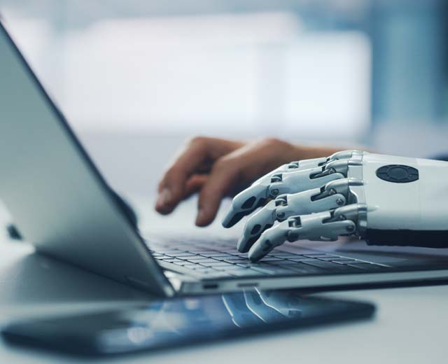 A human hand and a bionic hand type on a laptop.