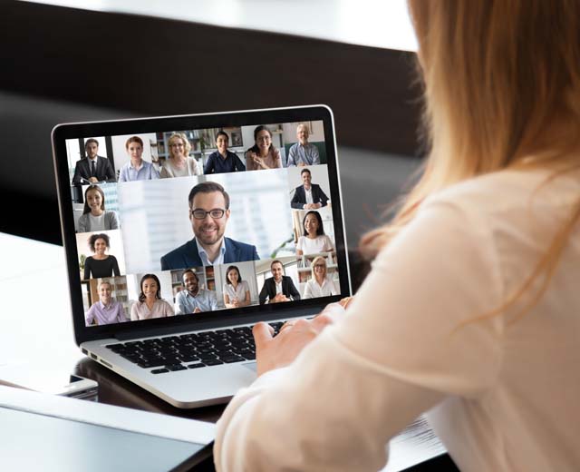 A person looking at a laptop screen showing a multi-person video meeting.