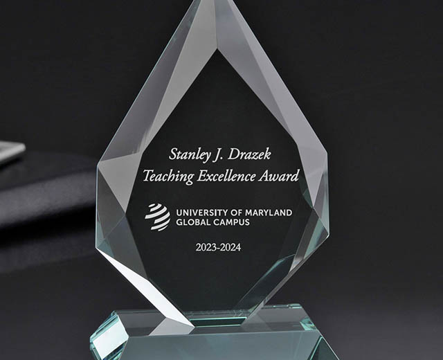 A picture of the Drazek Award trophy, which is glass and is etched with “Stanley J. Drazek Teaching Excellence Award, University of Maryland Global Campus, 2023-2024”.